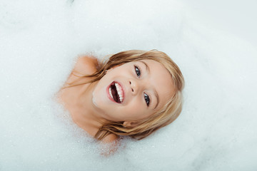 top view of happy kid taking bath and looking at camera at home