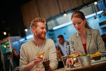 Cheerful couple in love sitting in restaurant for dinner. Woman is preparing to eat while man looking at her and holding glass of wine.