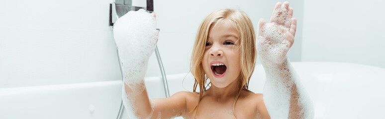 panoramic shot of kid with opened mouth and bath foam on hands