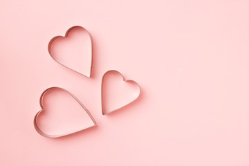 3 cutters cookies in heart shape on pastel pink background. Concept Valentine's card. Top view, copy space for text.
