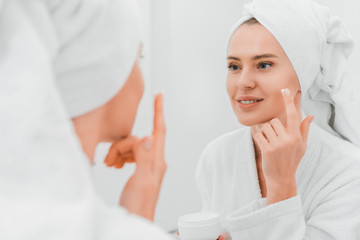 Selective focus of woman applying cosmetic cream in bathroom