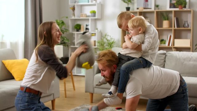Young dad crawling on floor carrying cute small child sons on back