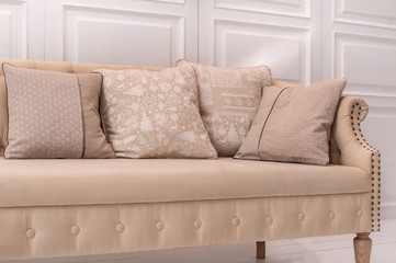 Luxury design elements: beige cushions with Christmas pattern on beige old style couch in white room