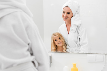Fototapeta premium selective focus of happy mother and cute daughter looking at mirror in bathroom