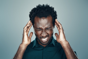 Frustrated young African man making a face while standing against grey background