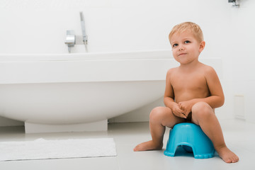 adorable toddler boy sitting on blue potty near bathtub