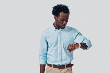 Handsome young African man checking the time while standing against grey background