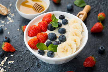 Delicious, healthy and balanced Breakfast of oatmeal with berries and fruit in a plate on the left on a concrete background. Horizontal orientation.