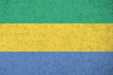 Gabon flag depicted in bright paint colors on old relief plastering wall. Textured banner on rough...