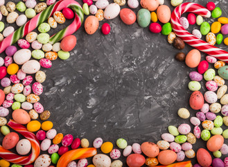 Colorful frame of multicolored candies on a black concrete background. Circle copy space, top view.