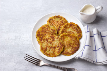 Traditional latkes fritters with sour cream on a light gray textured background with free space, top view