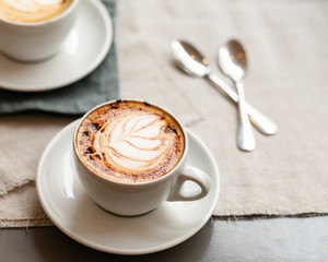 Every day morning routine: two cups of delicious creamy cappuccino, romantic breakfast for couple. Sift day light, close up, natural cotton background