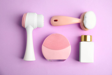 Flat lay composition with face cleansing brushes on violet background. Cosmetic tools