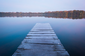 Old, wooden pier with frost surface into blue, calm lake on cloudy autumn morning with forest in background, Eutin, Schleswig-Holstein, Germanywinterday