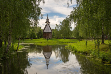 Obraz premium The old wooden Church is surrounded by birches on the shore of the pond. Kostroma, Russia.