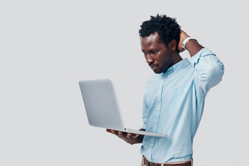 Handsome young African man using laptop while standing against grey background