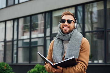 Smiling blind man in headphones holding book on urban street