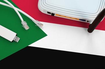 Sudan flag depicted on table with internet rj45 cable, wireless usb wifi adapter and router....