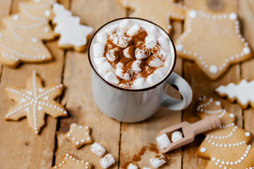 Fototapeta na wymiar Winter hot drink: white mug with hot chocolate with marshmallow and cinnamon. Cozy home atmosphere, festive holiday mood. Rustic style, wooden background. Homemade gingerbread cookies, white icing
