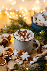 Winter hot drink: white mug with hot chocolate with marshmallow and cinnamon. Cozy home atmosphere, festive holiday mood. Rustic style, wooden background. Homemade gingerbread cookies