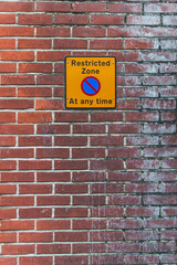 Fototapeta premium picture of a restricted zone sign on a old orange brick wall. Yellow sign, black letters, blue circle crossed out.