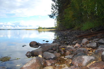 Fototapeta na wymiar View of the stones beginning the entrance to the river on the background of the sky reflected in the water. Shooting in 2014 in the Republic of Karelia, Russia.