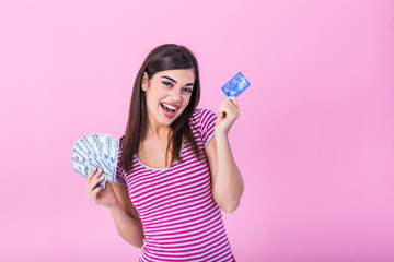 Portrait of a girl in a stripe t-shirt standing on a pink background. Model looks at the camera showing bank card and a bundle of dollars with dreamy look