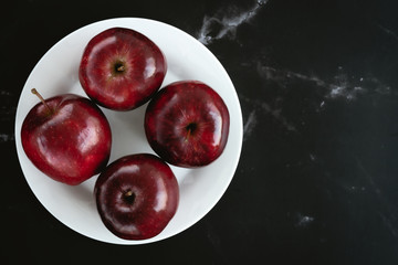 fresh juicy red apples on white plate on black marble surface. Top view flat lay composition. Space for text template