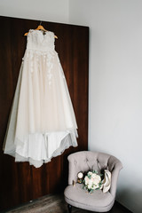 The bridal style vintage elegant dress with lace on brown wooden cabinet. Bride's Preparations. Wedding Morning. Stylish bouquet of flowers of the bride on retro armchair, shoes.