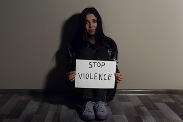 Abused young woman with sign STOP VIOLENCE near beige wall