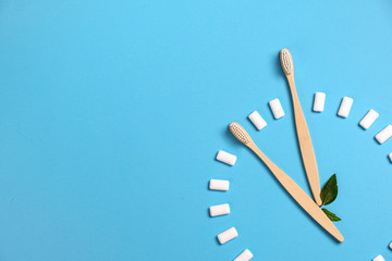 Dental care. Two wooden bamboo eco friendly toothbrushes, green leaf and chewing gum in the form of hours on a blue background. Eco friendly and reuse concept. Flat lay, top view, copy space