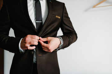 Man fastens the buttons. The groom in a suit, shirt, tie is standing on white background. Close up.
