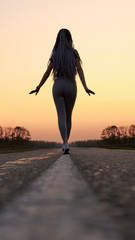 Silhouette of a sports girl, with African pigtails, walking along the dividing strip of the road.