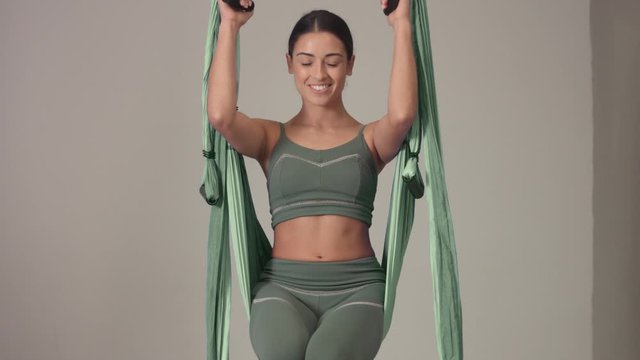 tilted plan of female aerial yoga teacher begins her class and jump into a hammock smiling