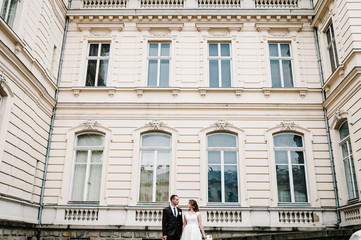 Portrait the groom and bride stand near ancient restored architecture, old building, old house outside, vintage palace outdoor. Romantic love in vintage atmosphere street.