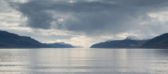A view across Loch Ness looking down the length of the lake with rocks inn the foreground and dark clouds above, in Scotland, UK