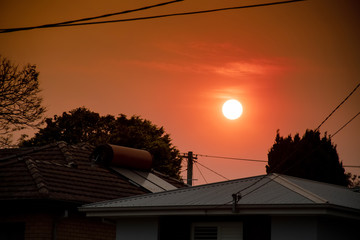 Australian bushfire: smoke from bushfires covers the sky and yellow and red sunset above the roofs...