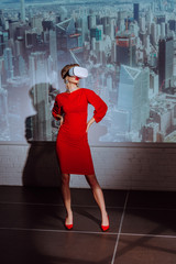 stylish woman with hands on hips in red dress and virtual reality headset on city background