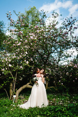 Wedding couple embracing and kissing in park on background of pink and purple flowers of magnolia and greens. Wedding location on the ceremony.