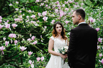 Stylish bride and groom are getting married on the wedding ceremony near the magnolia tree.