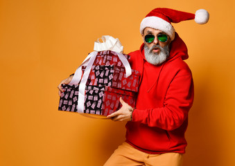 Popular elderly man or mature old men in a Santa Claus hat and sunglasses happy walks with New Year's gifts hurry for xmas party - Powered by Adobe