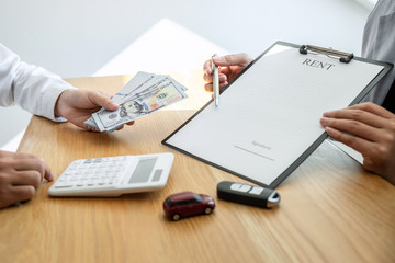 Car rental and Insurance concept, Young salesman receiving money and giving car's key to customer after sign agreement contract with approved good deal for rent or purchase