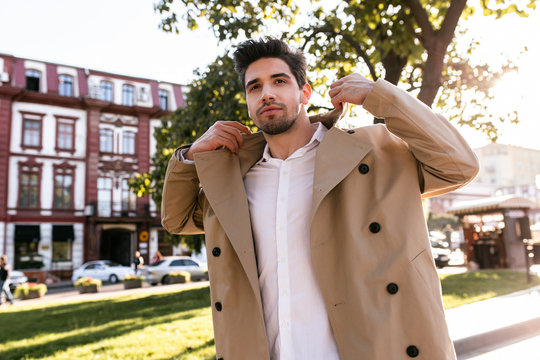 Portrait of confident stylish man in trench coat happily walking through street
