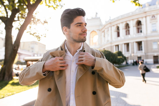 Portrait of attractive confident casual man in trench coat happily walking through street