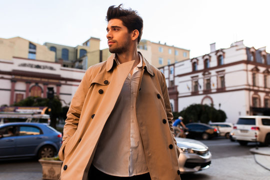 Young Attractive Stylish Man In Trench Coat Thoughtfully Looking Aside On Street