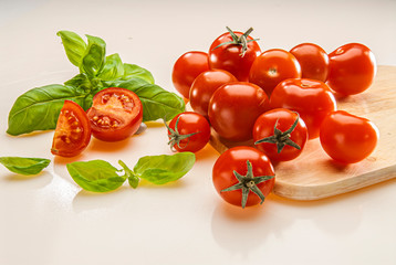 Tomaten auf einem Brett, daneben aufgeschnittene Hälften mit Basilikum auf hellem Grund