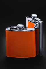 Two flask for alcohol. Steel flask with leather trim stand on a black background. Tanks for whiskey, rum, vodka and various alcohol.