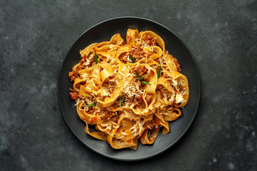 Pasta Bolognese with spices, Italian pasta dish with minced meat and tomatoes in a dark plate on a stone background