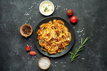 Pasta Bolognese with spices, Italian pasta dish with minced meat and tomatoes in a dark plate on a stone background