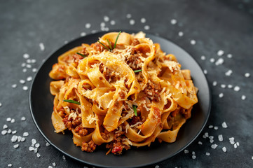 Pasta Bolognese with spices, Italian pasta dish with minced meat and tomatoes in a dark plate on a stone background